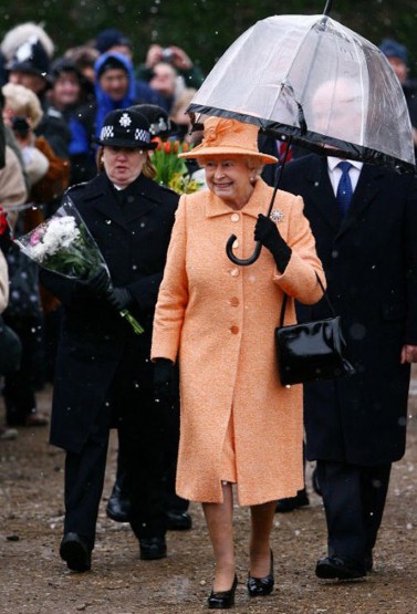 14. 下雨的时候，女王伊丽莎白二世(Queen Elizabeth II)也会注意雨伞与衣服的搭配，这件橘色大衣、橘色帽子搭配黑色手套、黑色挎包和黑边透明伞，也别具有一番情调。